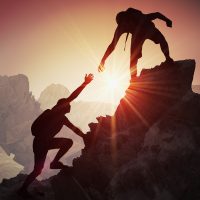 Silhouettes of two people climbing on mountain and helping.